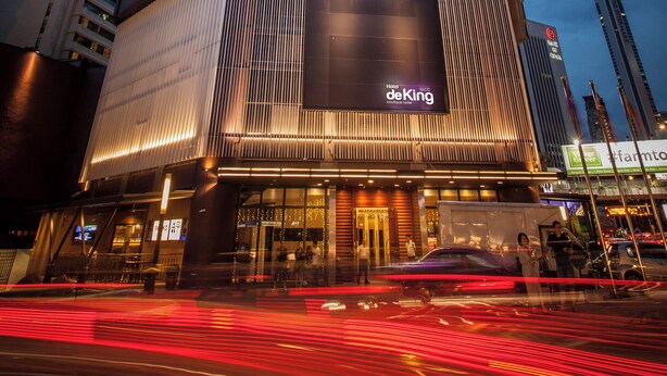 Un grand hôtel, reconnaissable à son imposante enseigne « deKing », doté d’une façade moderne et de fenêtres illuminées.
