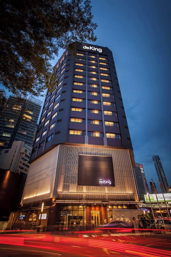 Un grand hôtel, reconnaissable à son imposante enseigne « deKing », doté d’une façade moderne et de fenêtres illuminées.