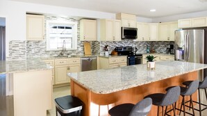 A modern kitchen with granite countertops, stainless steel appliances, and a central island with bar stools. - Spacious 4 bedroom Fort Myers house , Pool, great for Families, Sports or Golf! (Fort Myers)