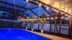 An outdoor swimming pool with a glass enclosure, string lights, and potted plants. - Spacious 4 bedroom Fort Myers house , Pool, great for Families, Sports or Golf! (Fort Myers)