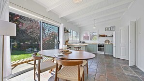 A spacious kitchen with a large island, a dining area with a round table and chairs, and a view of a garden through large windows. - Dora Cottage • Fireplace + Firepit • Walk to CBD (Orange)
