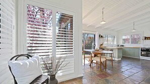 A spacious kitchen with a dining area, large windows with blinds, and a stone-tiled floor. - Dora Cottage • Fireplace + Firepit • Walk to CBD (Orange)
