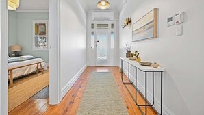 A hallway with a wooden floor, a white door at the end, a bench with a lamp, and a console table with decorative items. - Dora Cottage • Fireplace + Firepit • Walk to CBD (Orange)