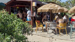 Un bar frente a la playa con mesas al aire libre y sombrillas de paja.
