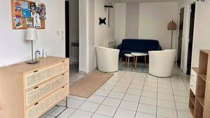A modern living room with a blue sofa, white armchairs, a wooden dresser, a bulletin board, and a ceiling light fixture. - L'Abri Châtelaillonnais, sleeps 7, close to the beach and market. (Châtelaillon-Plage)