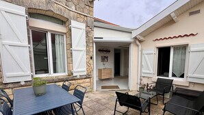A patio with a table and chairs, a potted plant, and a stone building with a door and windows. - L'Abri Châtelaillonnais, sleeps 7, close to the beach and market. (Châtelaillon-Plage)