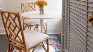 Un coin repas avec une table ronde, deux chaises en osier, un vase de fleurs jaunes et un tableau abstrait moderne accroché au mur.