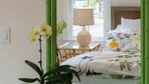 Une pièce avec un miroir encadré de bambou vert, un lit avec une literie à motifs floraux, une lampe de chevet et une plante en pot.