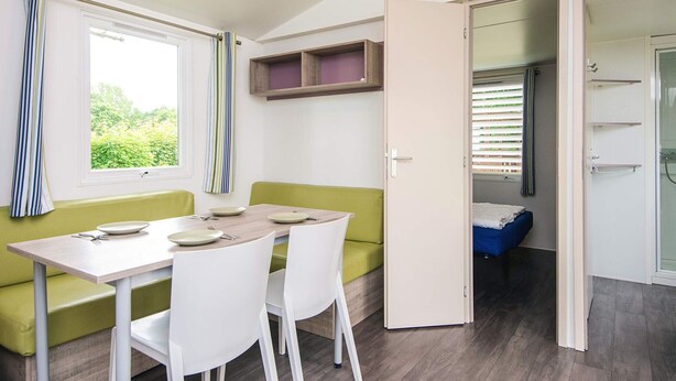 A compact room with a dining table and chairs, a green sofa, a wardrobe, and a shower area. - 4 Person Holiday Park Home in Jelling (Jelling)
