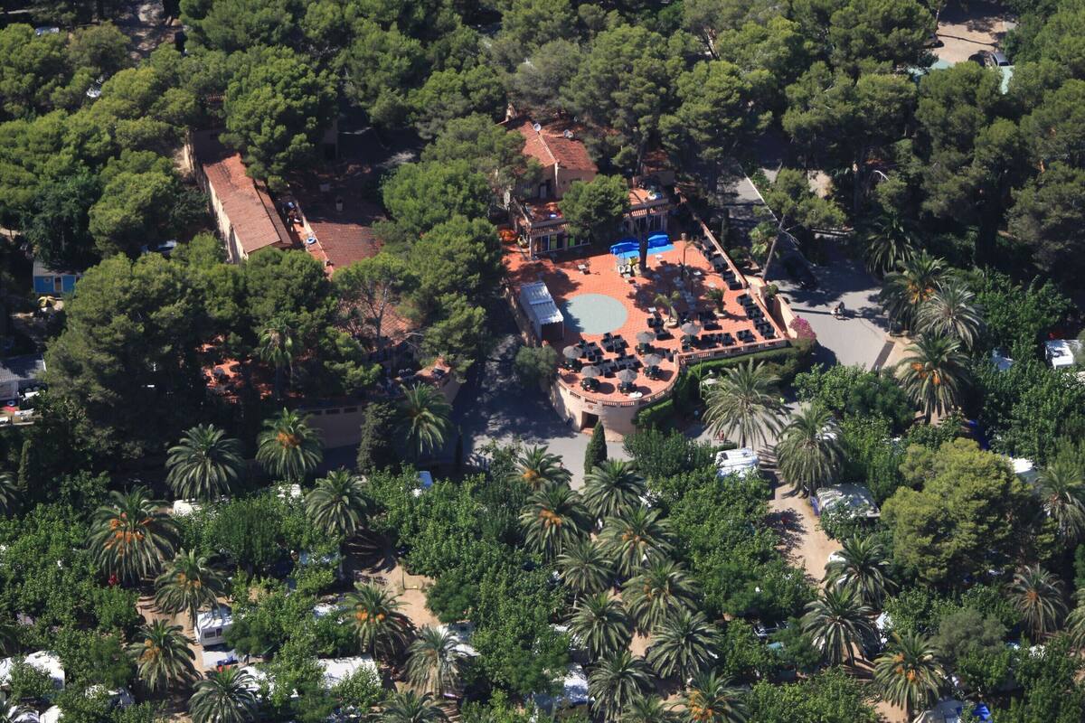 An aerial view of a resort with a central courtyard, surrounded by dense greenery and palm trees.