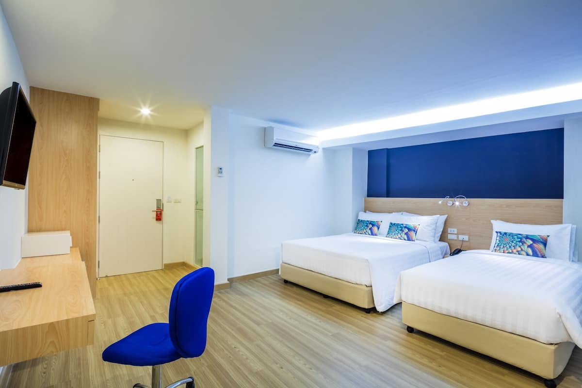 A hotel room with two beds, a desk, a chair, and an air conditioning unit.