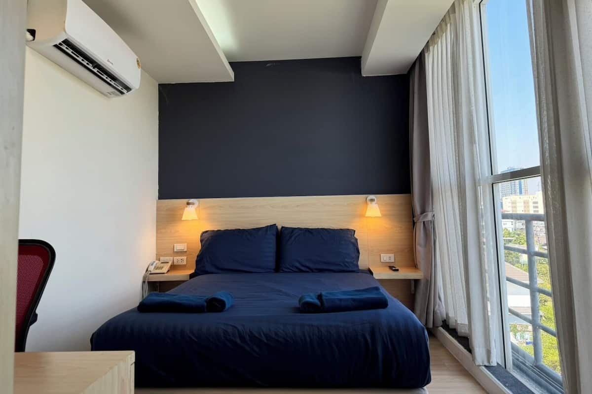 A modern hotel room with a large bed, two bedside lamps, a desk, and a window with curtains.