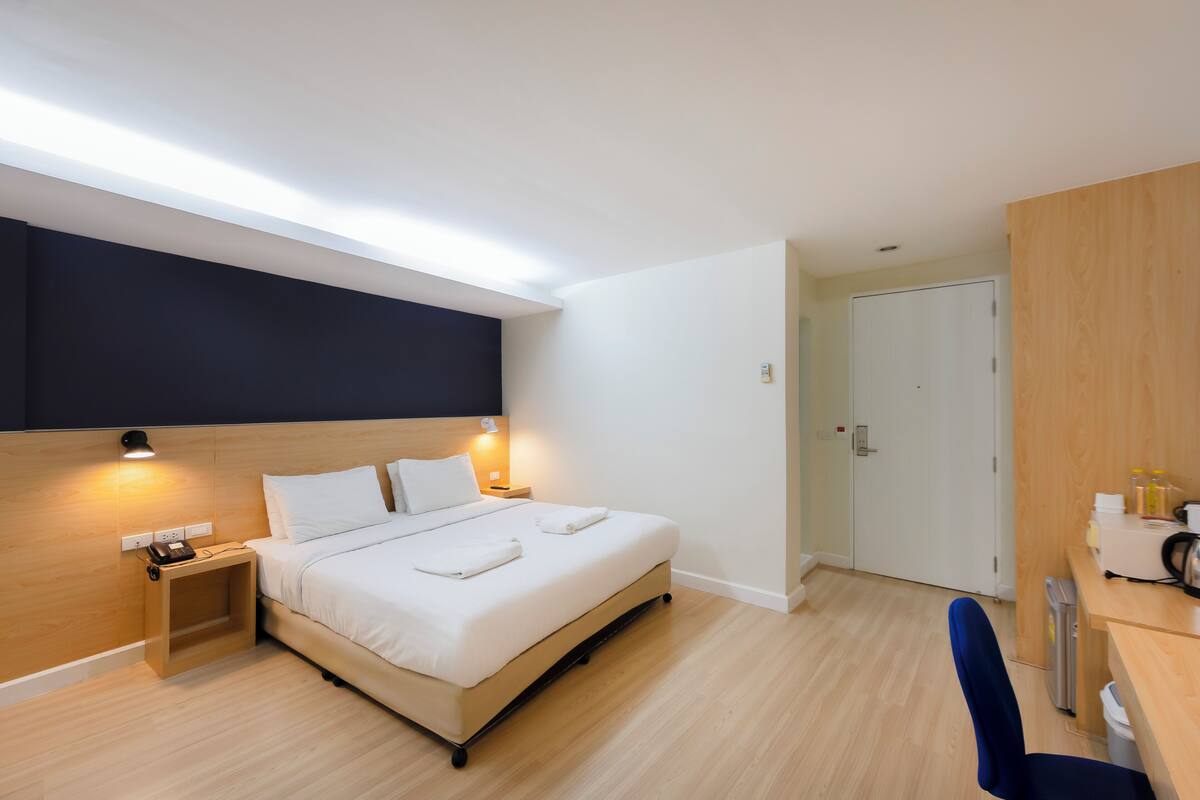 A modern hotel room with a bed, bedside tables, a desk, and a wardrobe.