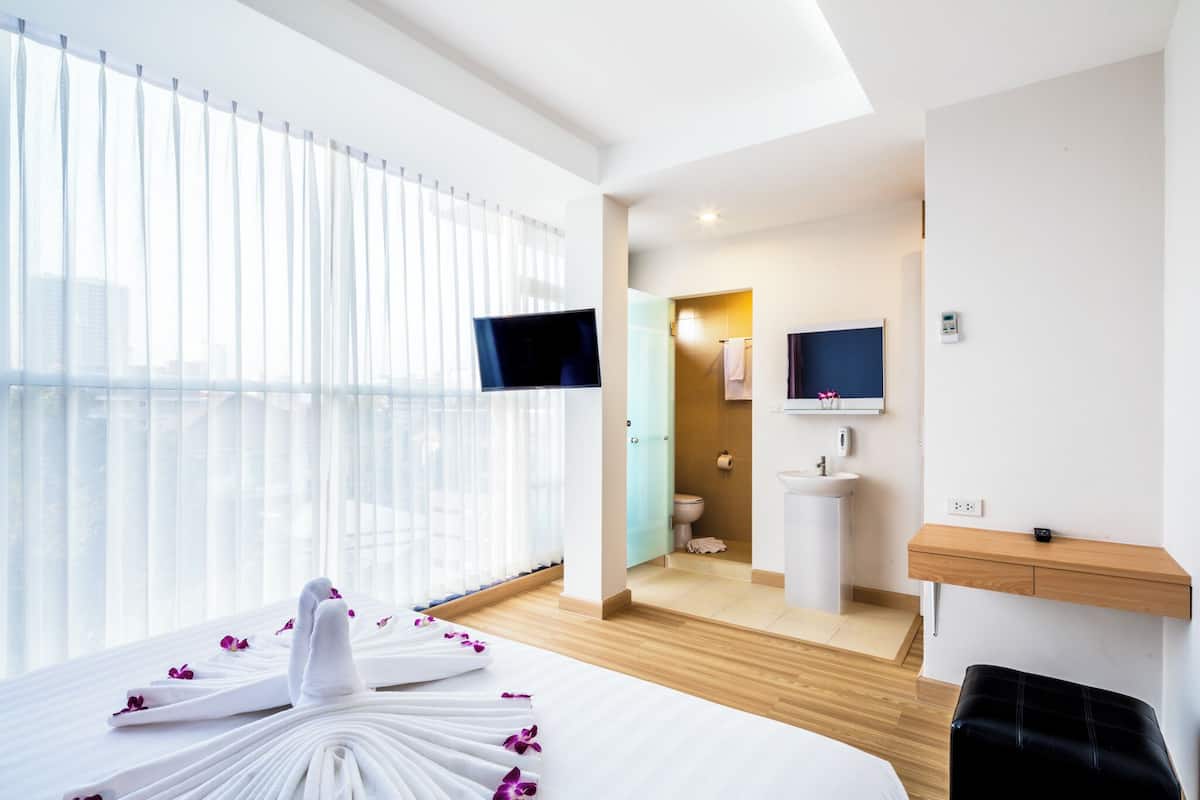 A hotel room with a bed, a TV, a bathroom, and a wooden shelf.
