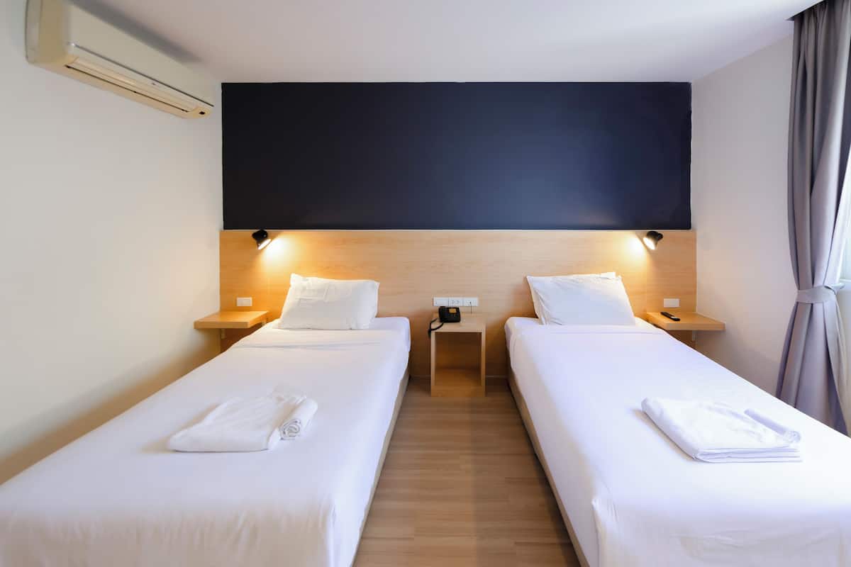 A hotel room with two single beds, a large dark wall, and a wooden floor.