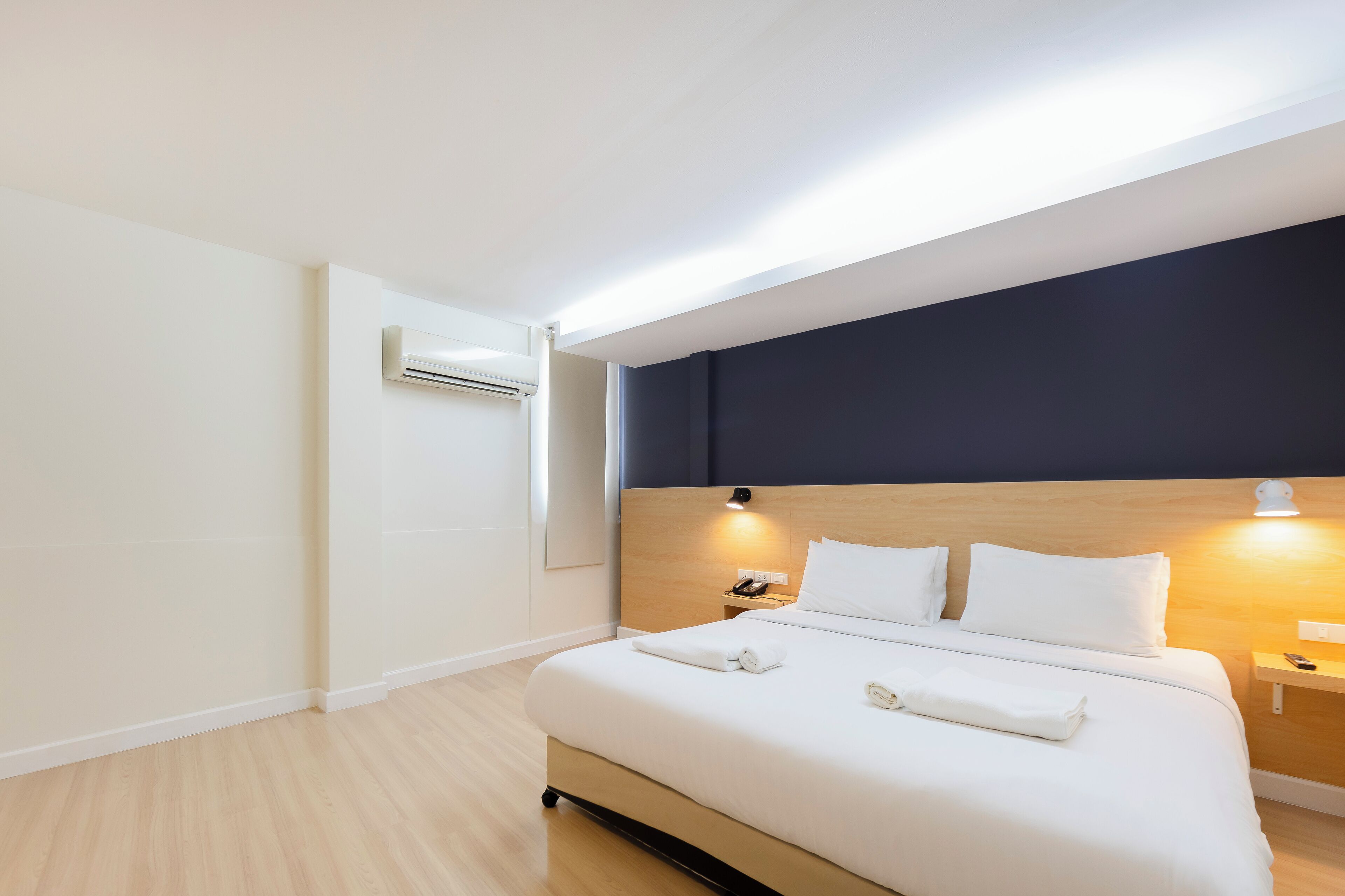 Habitación de hotel con una cama grande, mesitas de noche, un equipo de aire acondicionado y una pared decorativa oscura.