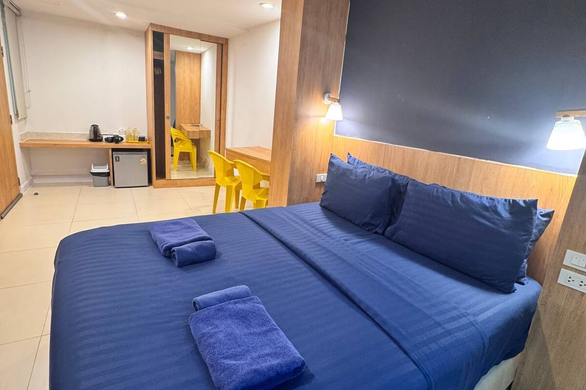A hotel room with a large bed, a desk, a chair, and a small kitchenette.