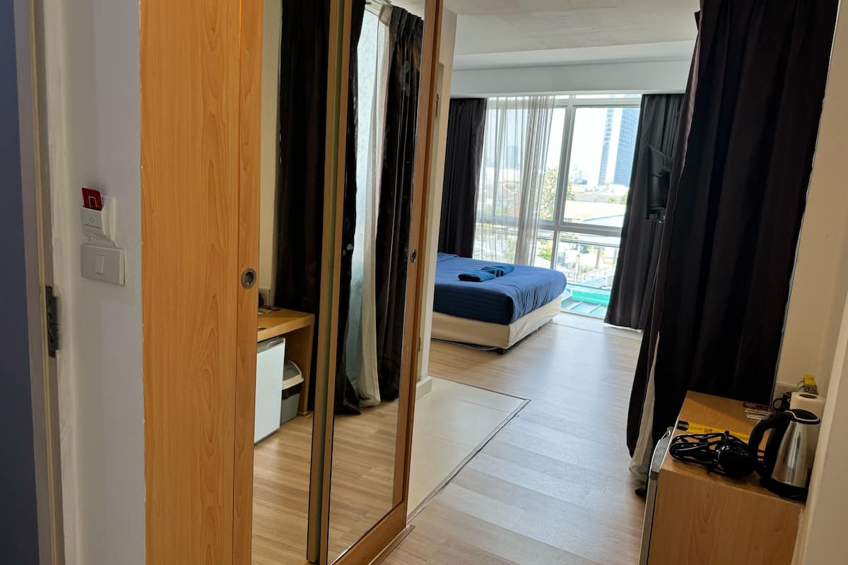 A bedroom with a bed, a desk, and a view of the outside.