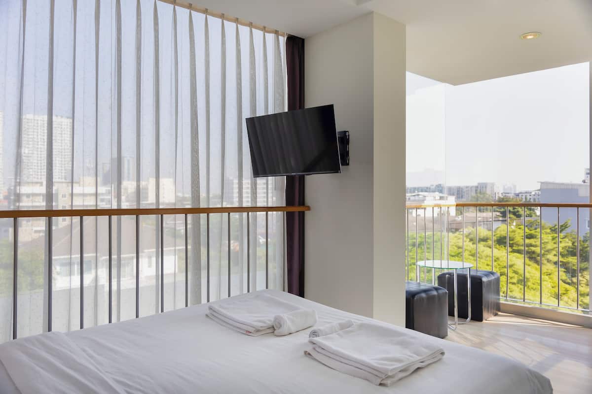 A modern hotel room with a large bed, a mounted TV, and a balcony with a city view.
