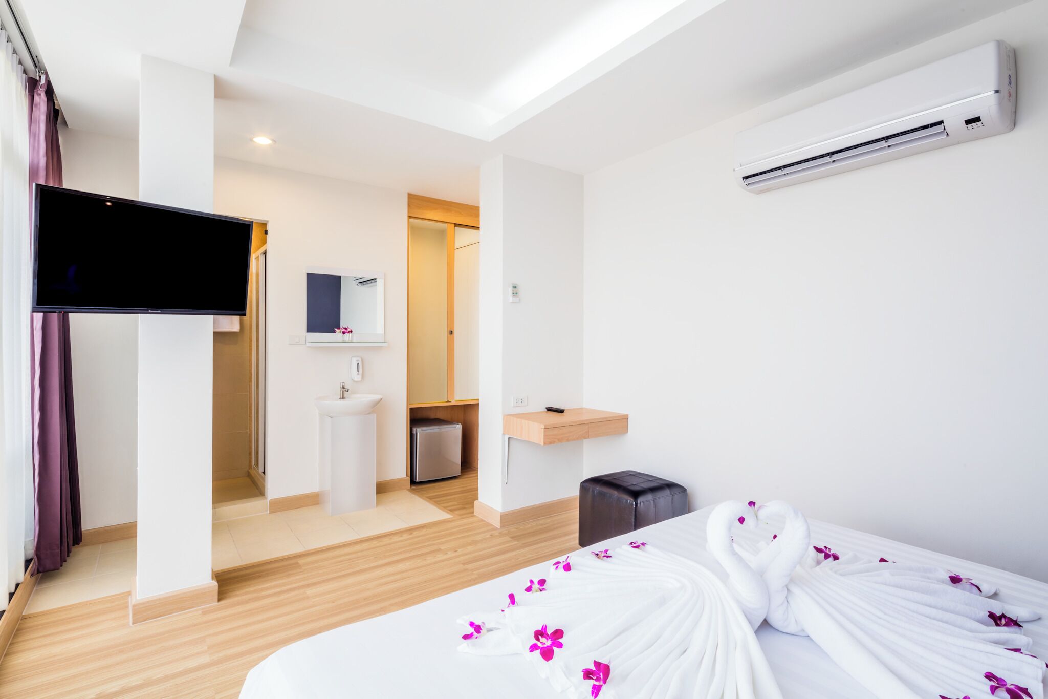 A hotel room with a bed, a TV, a bathroom, and a kitchenette.