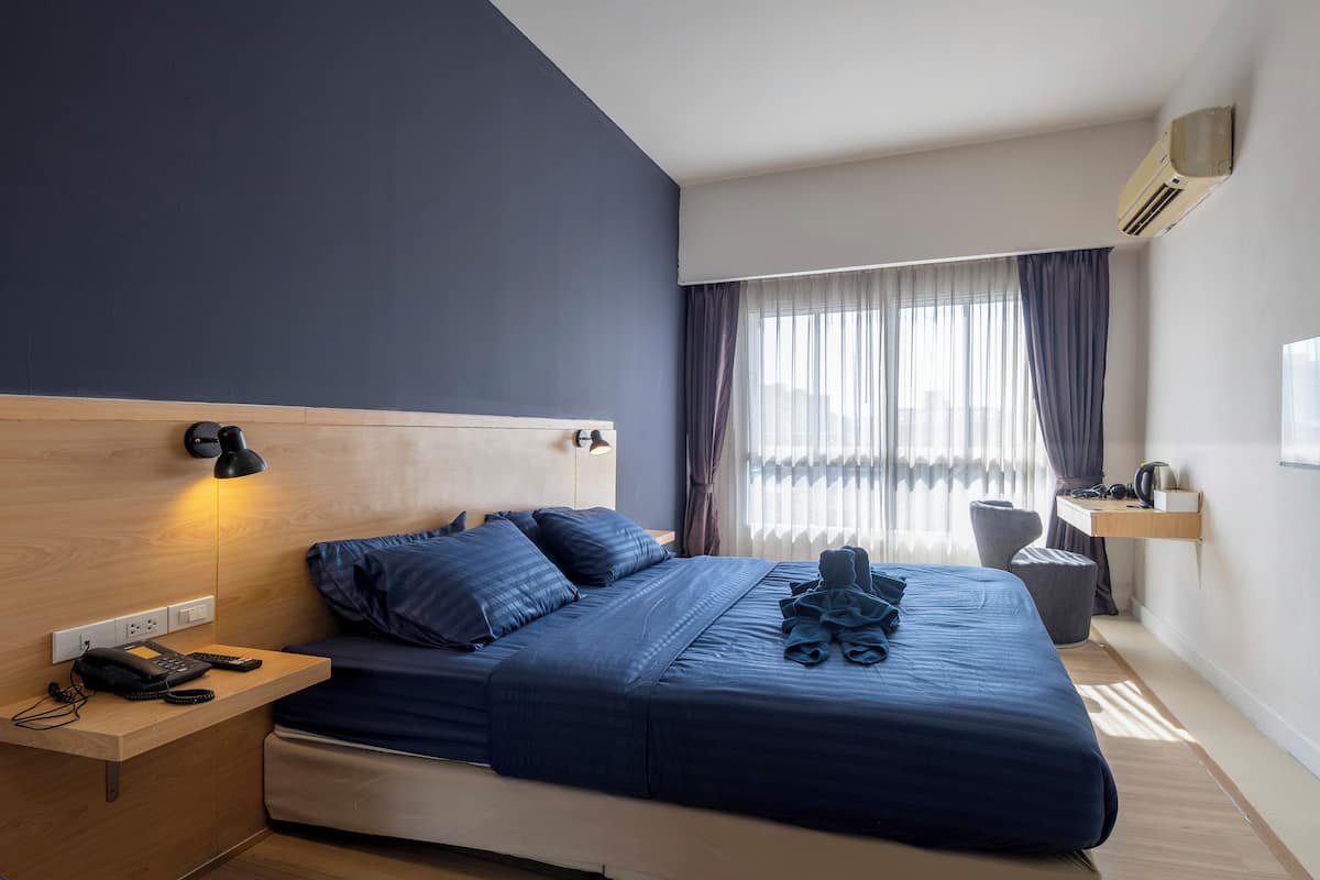 A modern hotel room with a large bed, bedside lamps, a desk, and a window with curtains.