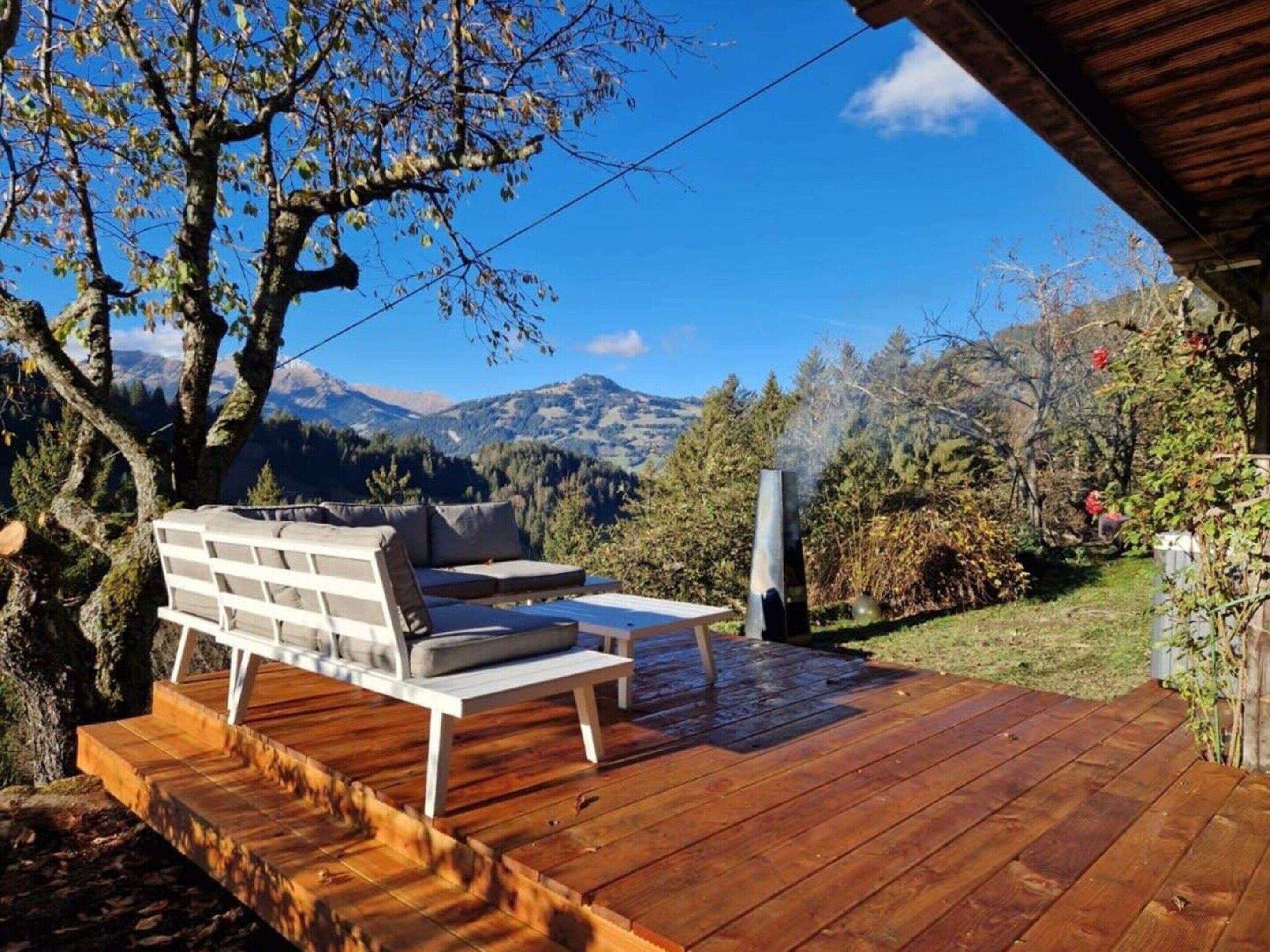 A wooden deck with outdoor furniture, a view of mountains, and a tree.