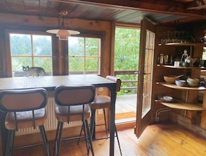 A rustic wooden interior with a large table, chairs, and a view of greenery outside. - Chalet in Rougemont Near Ski Slopes (Rougemont)