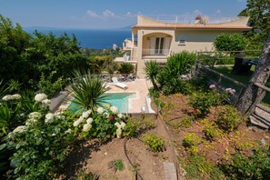 Eine Villa mit Swimmingpool, umgeben von üppiger Vegetation und Blick auf das Meer.