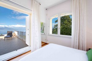 Un dormitorio con un ventanal grande, un balcón y vista al mar.