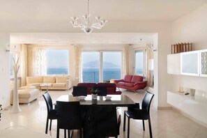 Ein geräumiger Wohnbereich mit Esstisch, zwei Sofas und einem großen Fenster mit Meerblick.