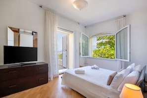 Un dormitorio con cama, televisor en una cómoda, ventana con cortinas y vistas al verdor exterior.