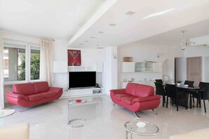 Ein modernes Wohnzimmer mit zwei roten Sofas, einem Glastisch, einem Flachbildfernseher und einem Essbereich mit einem schwarzen Tisch und Stühlen.