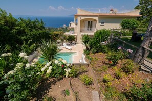 Una villa con piscina, rodeada de exuberante vegetación y vistas al mar.