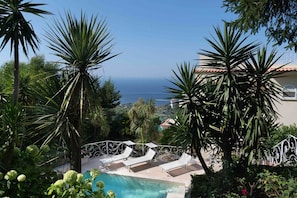 Ein Poolbereich mit Liegestühlen und Blick aufs Meer.