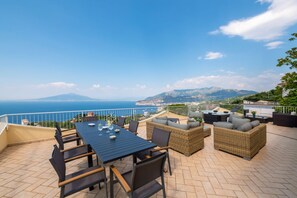 Eine Terrasse mit Tisch und Stühlen, Korbmöbeln und Blick auf das Meer und die Berge.