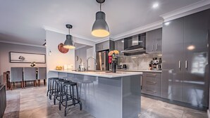Een moderne keuken met een groot kookeiland, barstoelen, roestvrijstalen apparatuur en hanglampen.