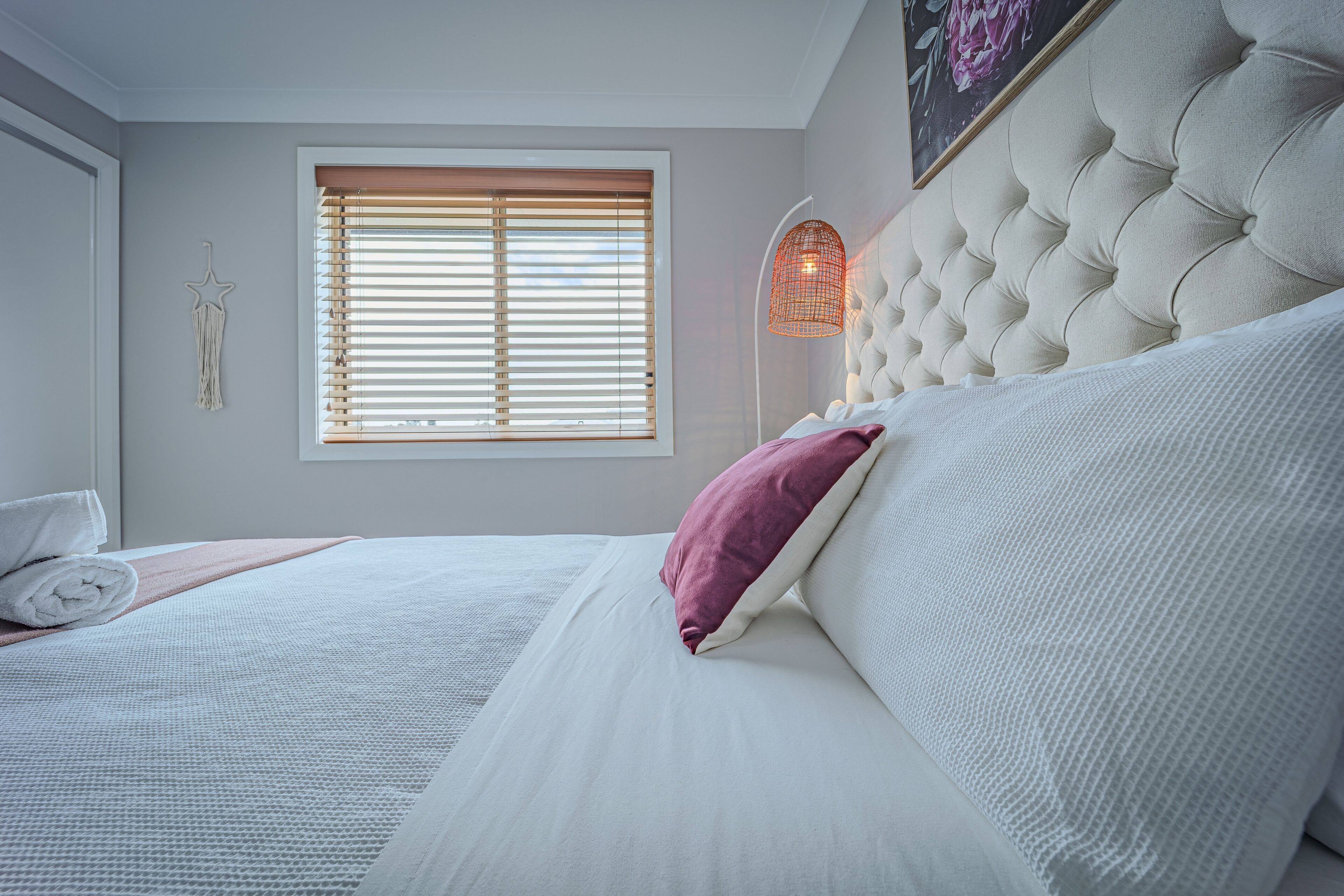 Un letto rifatto con cuscini bianchi e rosa, una decorazione a forma di stella e una finestra con persiane.