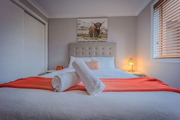 A neatly made bed with a white and orange blanket, a headboard with a picture of a bull, and a bedside lamp.