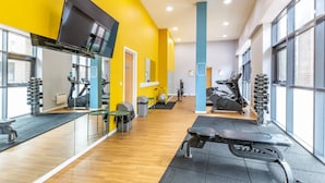 A modern gym with exercise equipment, large windows, and a bright yellow wall. - For Students Only Bryson Court (Newcastle-upon-Tyne)