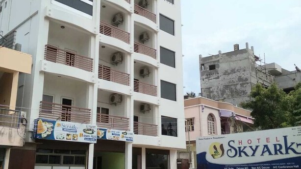 A multi-story hotel with balconies, a signboard for a restaurant, and a partially constructed building in the background. - Hotel skyark (Nagercoil)