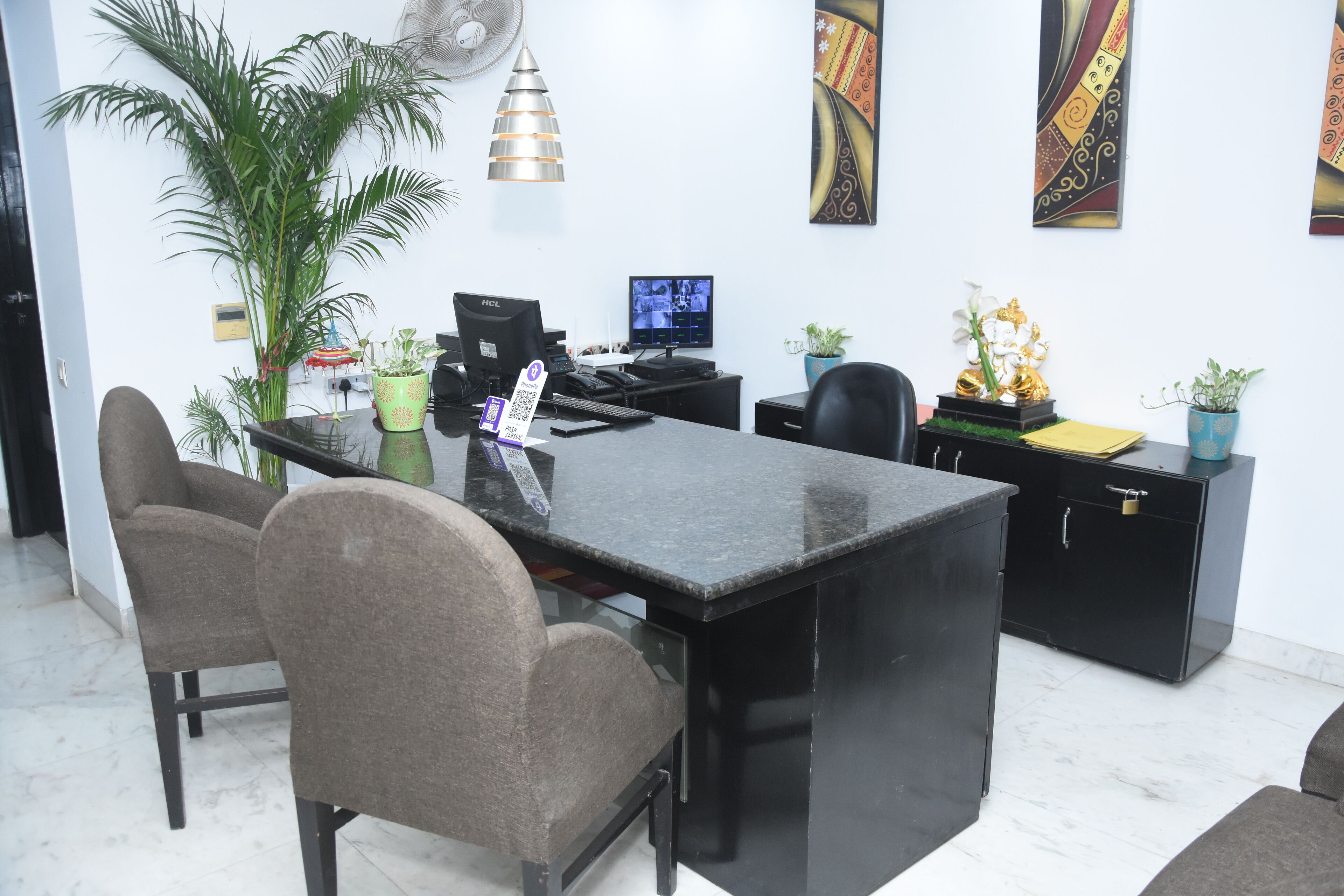 Una oficina moderna con un escritorio negro, dos sillas, una computadora y plantas decorativas.