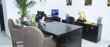 Una oficina moderna con un escritorio negro, dos sillas, una computadora y plantas decorativas.