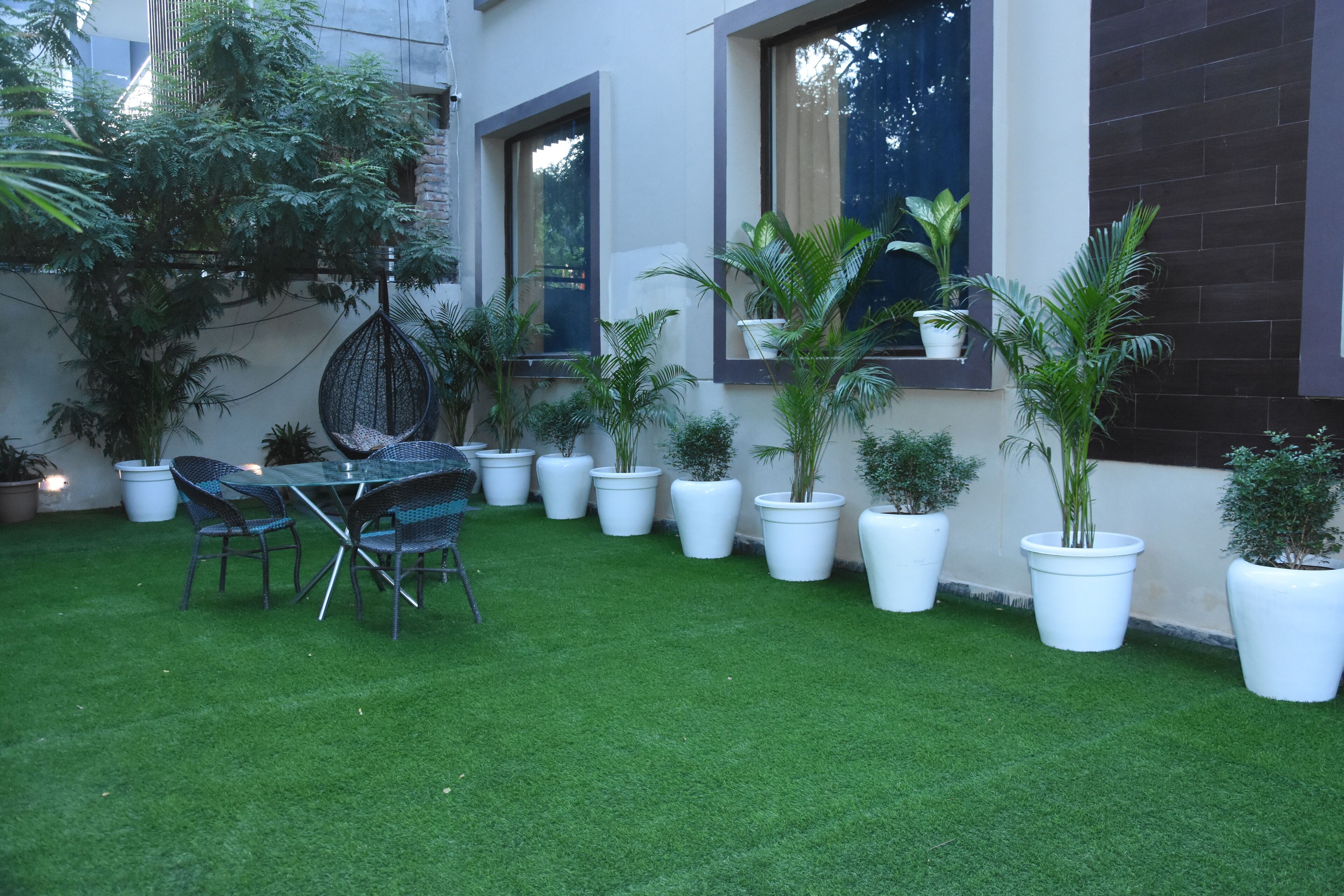 A patio area with a table and chairs, surrounded by potted plants and a grassy lawn.