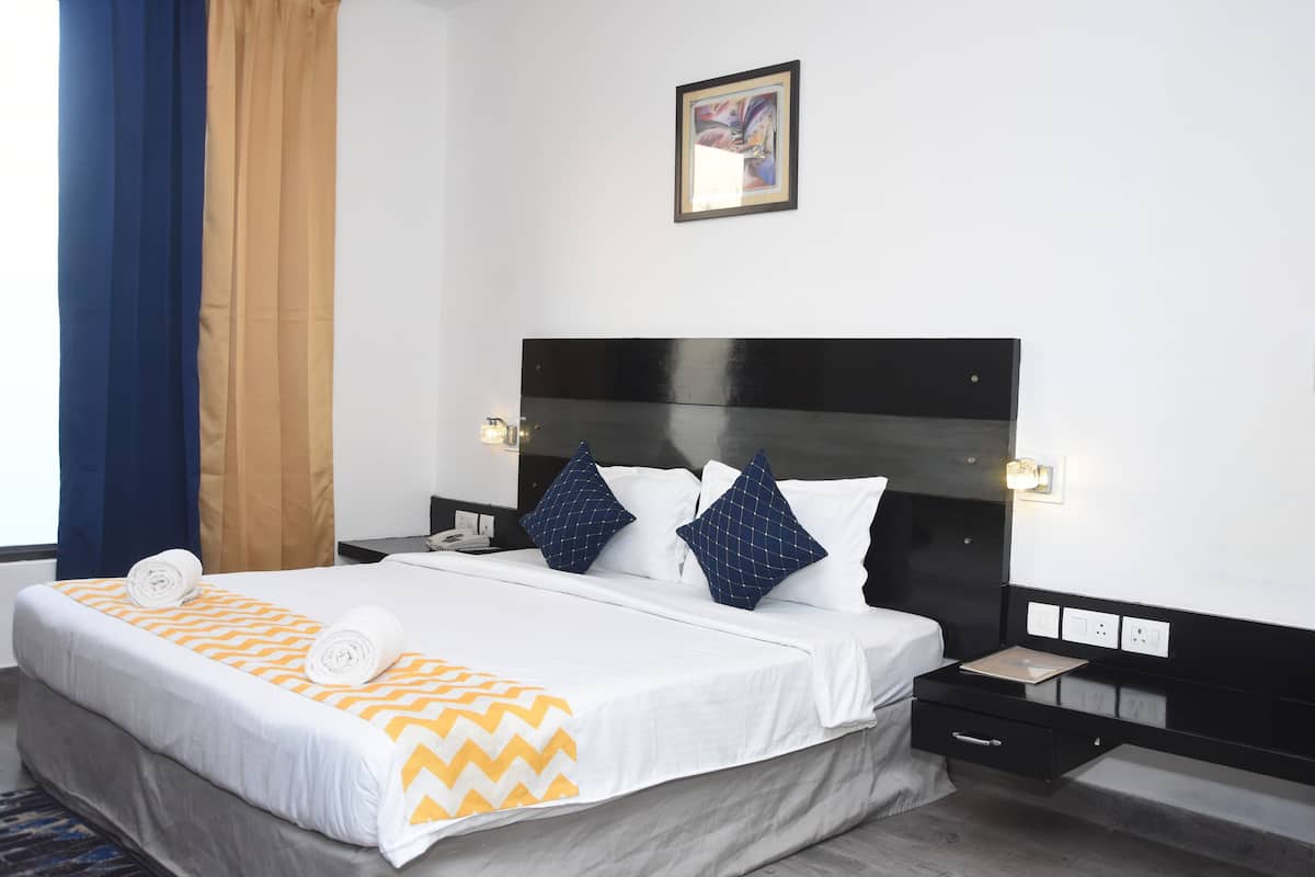 A hotel room with a bed, a nightstand, a wall-mounted light, and a painting.