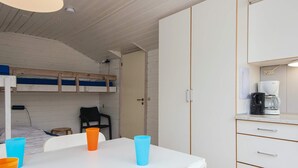 Ein kleines Zimmer mit Etagenbetten, einem Tisch mit Stühlen und einer Küchenzeile inklusive Kaffeemaschine.