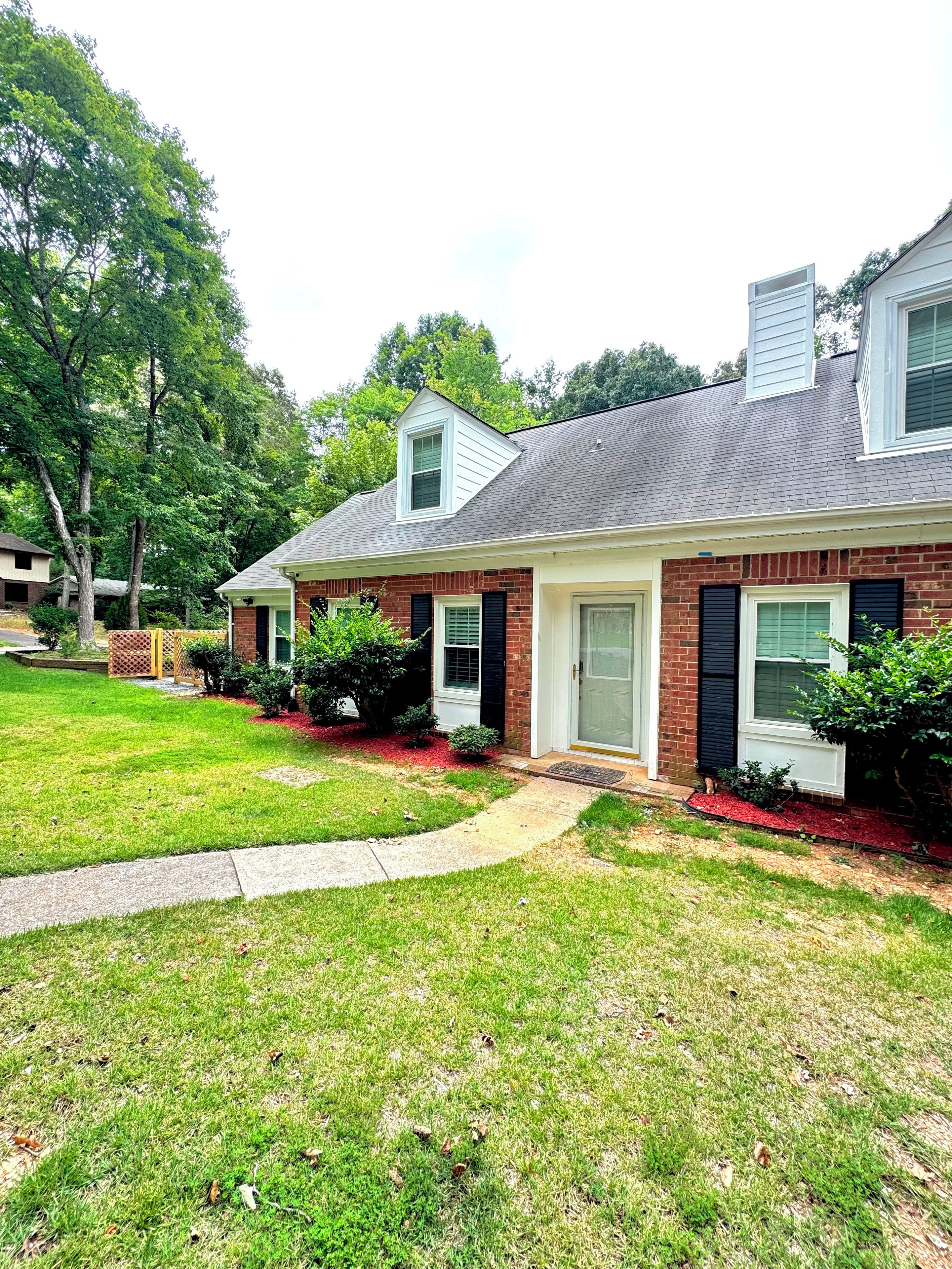 A two-story brick house with a front porch, a small attached garage, and a well-maintained lawn.