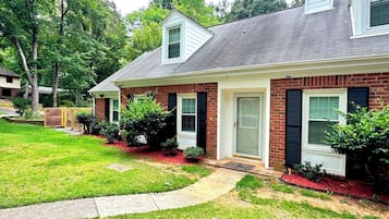 A two-story brick house with a front porch, a small attached garage, and a well-maintained lawn.