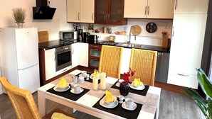 Une cuisine moderne avec des meubles blancs, un four à micro-ondes, une cuisinière et un évier. On y trouve une table à manger mise avec des assiettes, des tasses et un vase de fleurs.