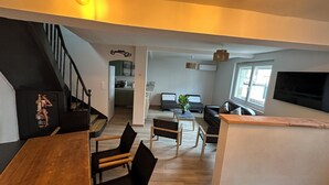 Ein moderner Wohnraum mit Treppe, Essbereich, Küche, einer Sitzecke inklusive Sofa und Pflanze sowie einem großen Fenster, das für natürliches Licht sorgt.