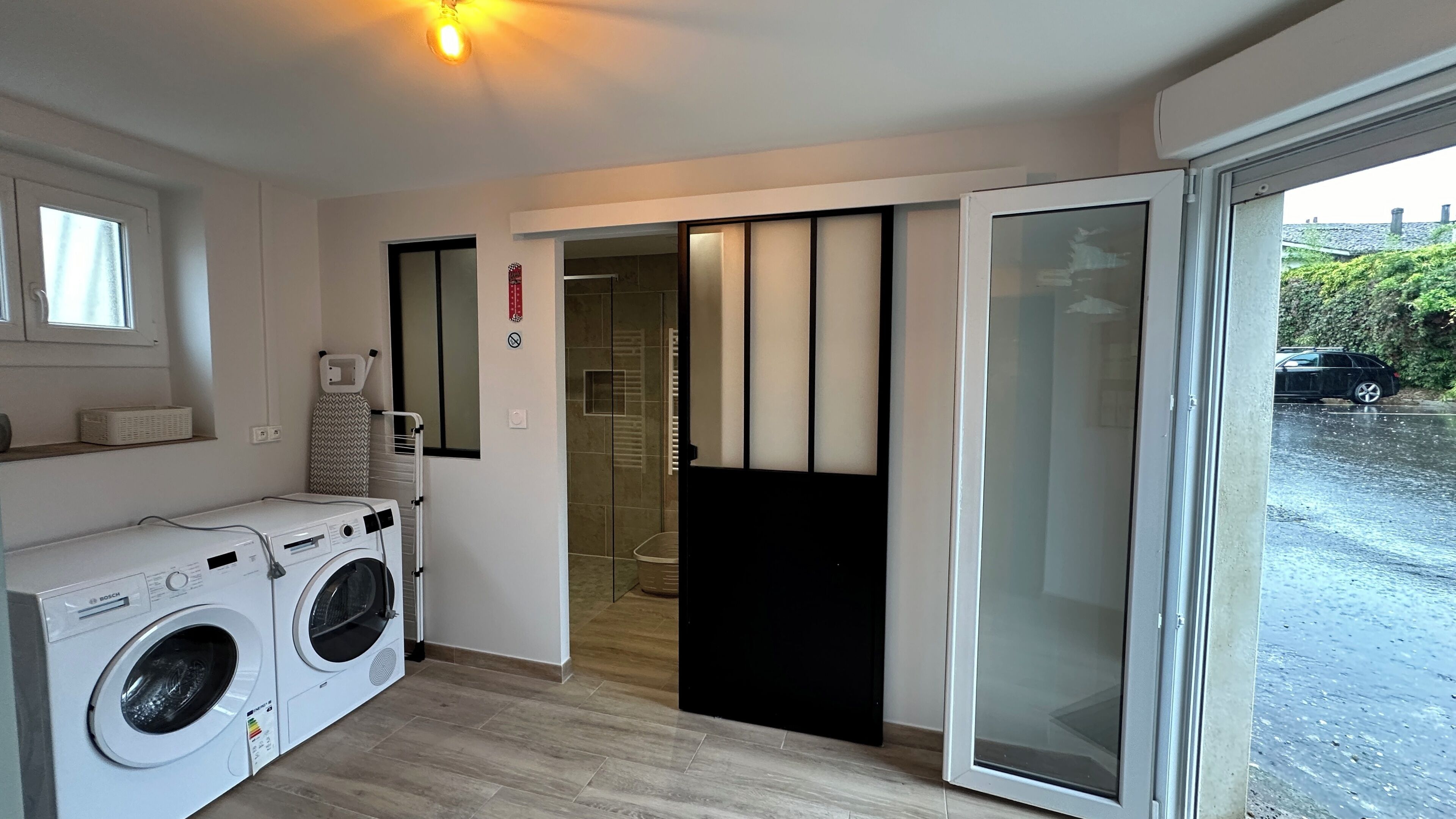 A laundry area with a Bosch washing machine, a drying rack, and a sliding glass door leading to a garage.